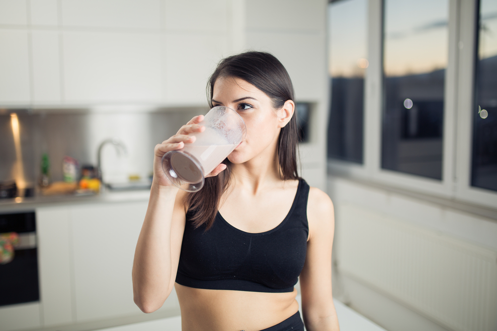 en tjej som dricker proteinpulver som är ett av dem bästa kosttillskotten för att gå ner i vikt med hemmaträning med